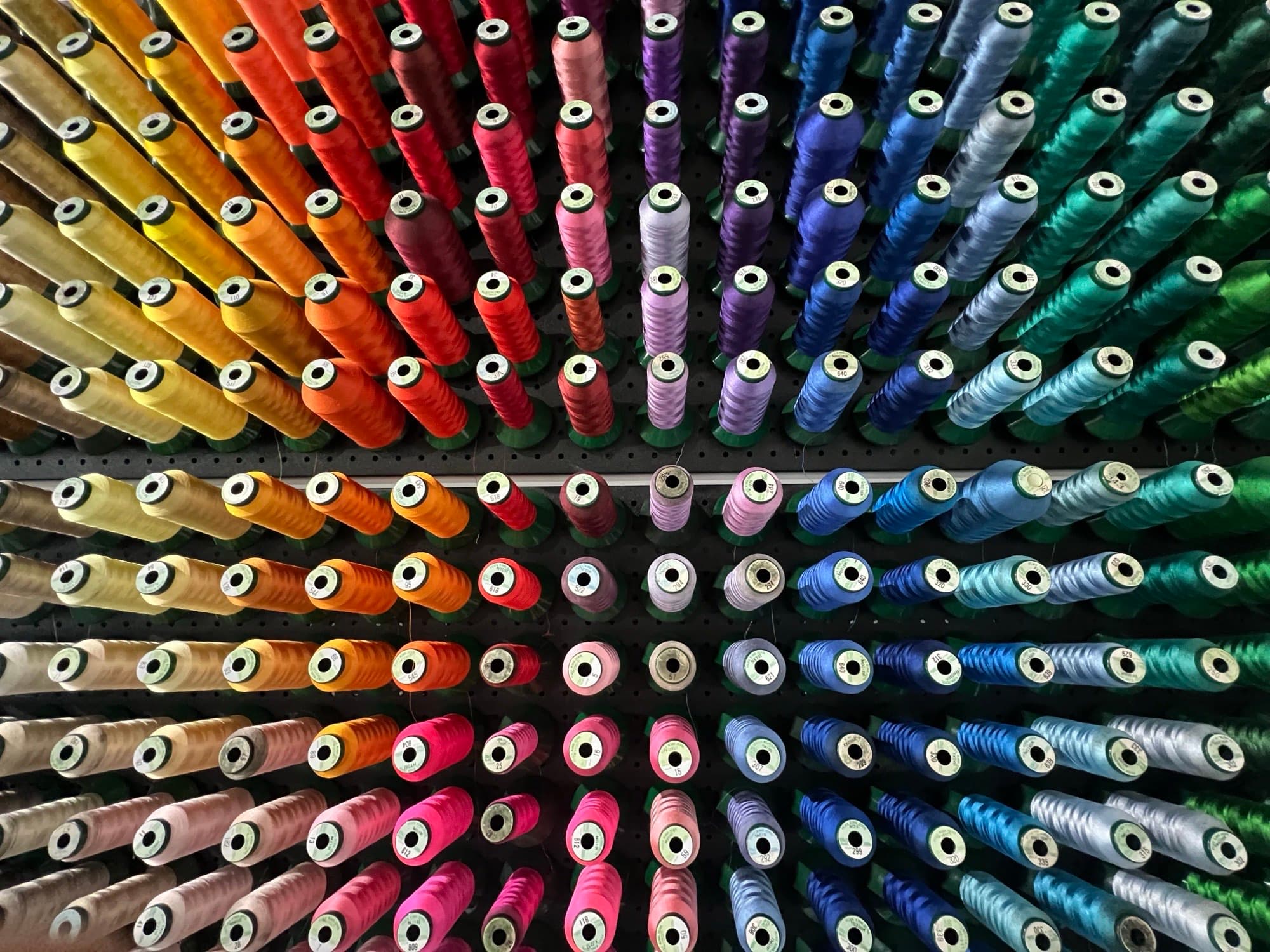 Wall of embroidery thread cones arranged in a rainbow colour spectrum at the SC Prints studio.