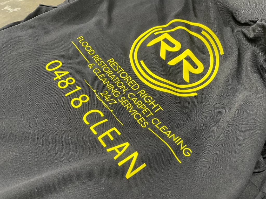 Dark grey garment with a yellow screen-printed Restored Right flood restoration and cleaning logo and phone number.